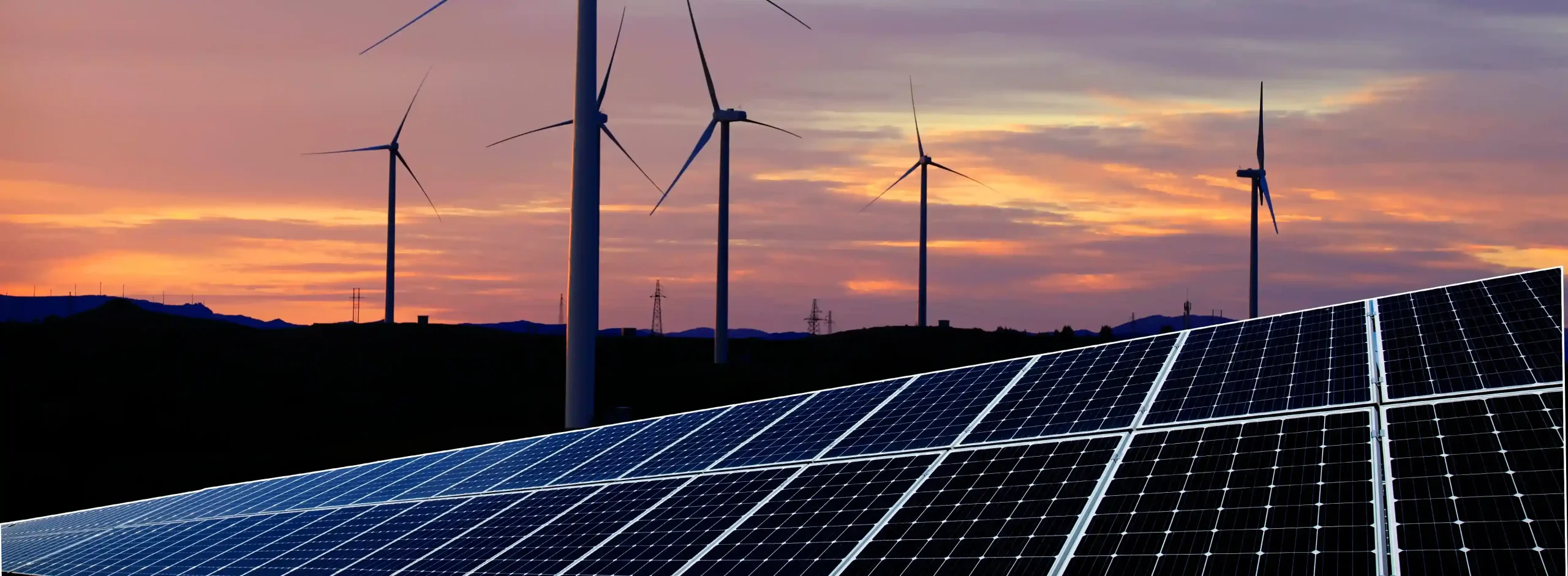Een foto met zonnepanelen en op de achtergrond windmolens en een zonsondergang